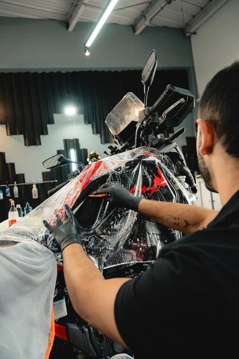 Manos con guante alisando la película de PPF sobre la superficie de una motocicleta.