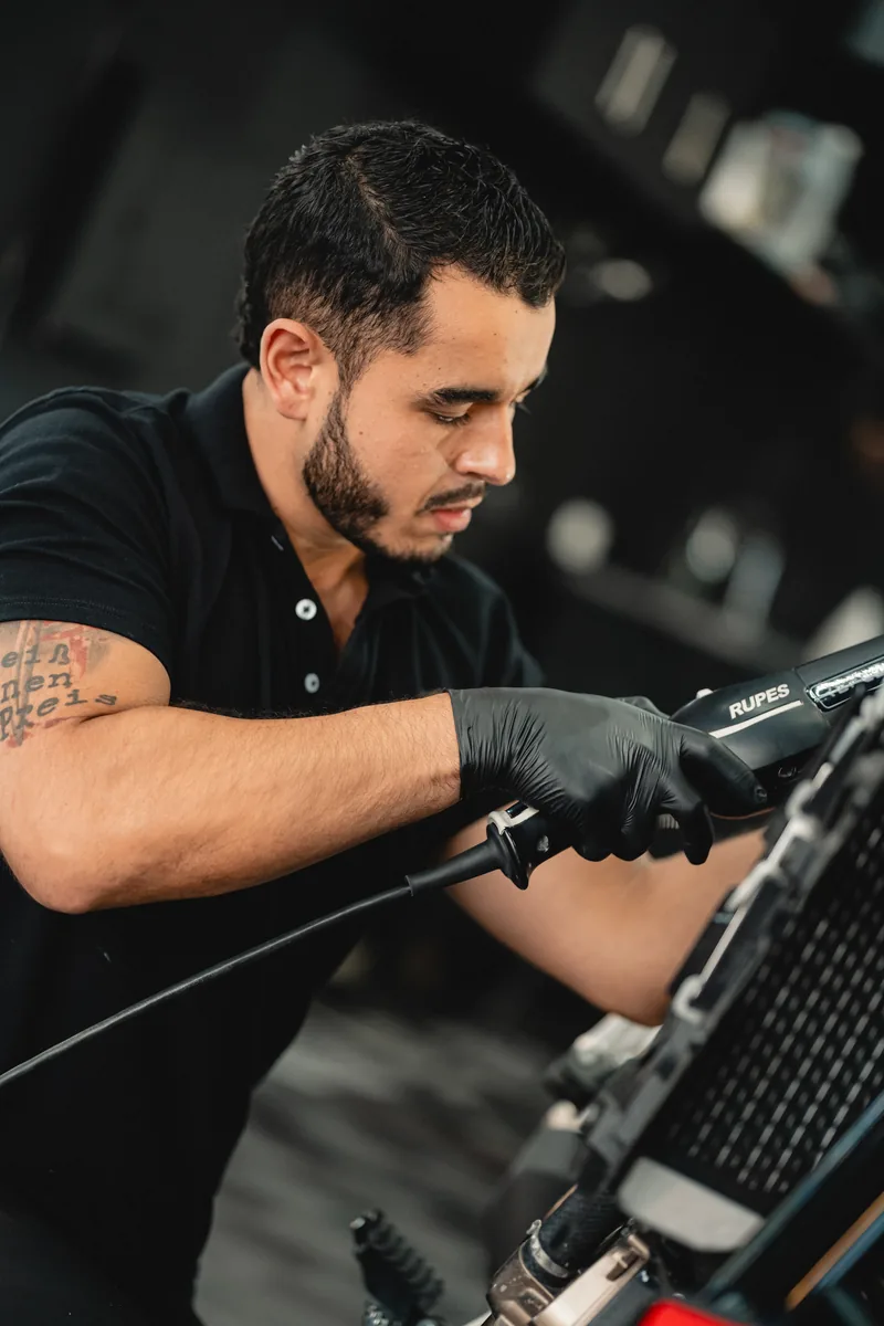 Técnico con pistola de calor trabajando sobre la parrilla frontal de un vehículo.